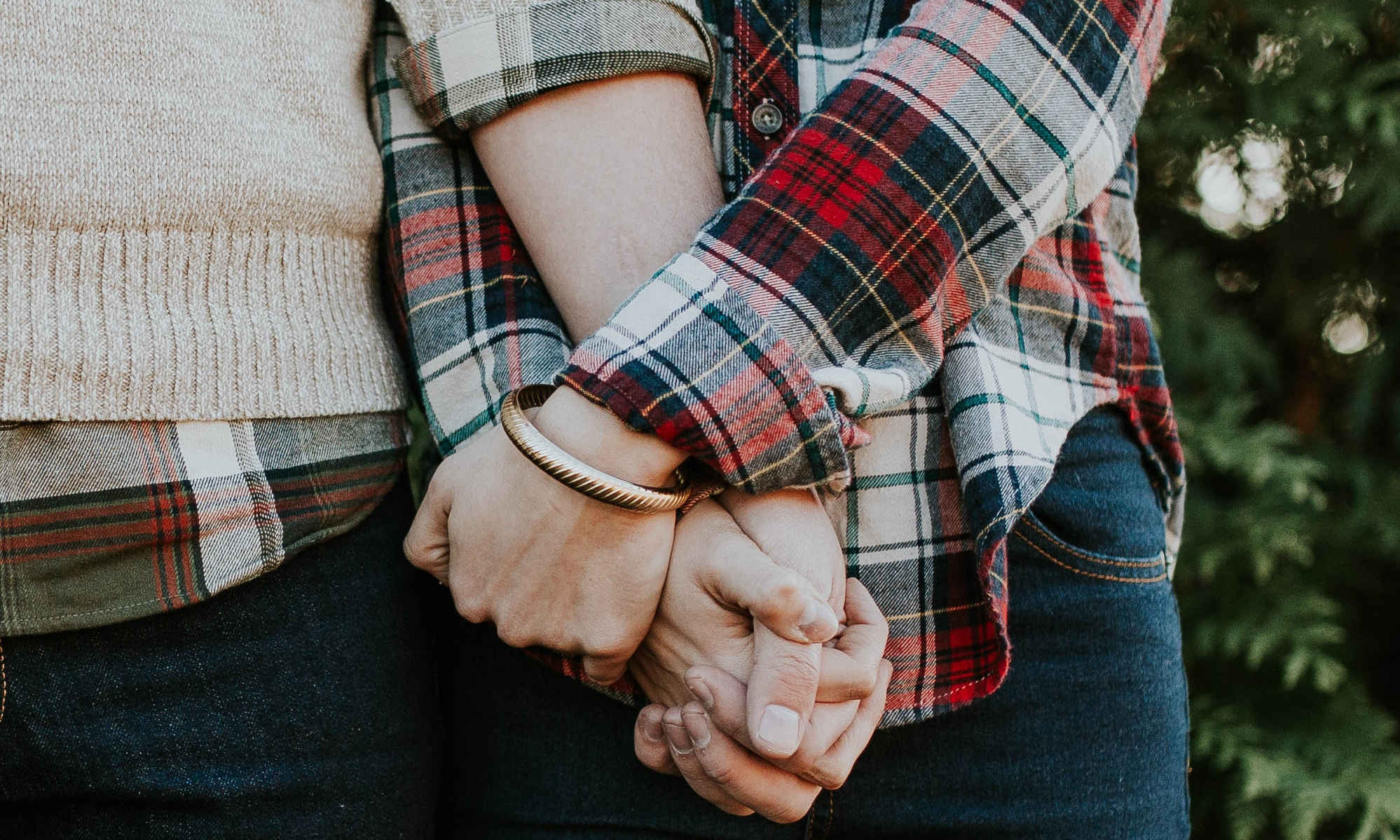 Picture of couple wearing flannel and holding hands in the forest